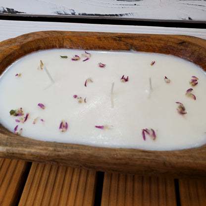Candle with flower petals in a wooden dish on a wooden surface