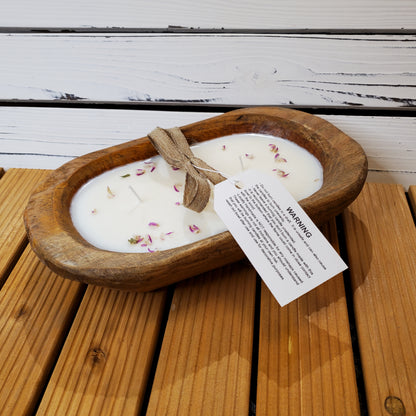 Candle in a wooden dish with rose petals on a wooden surface