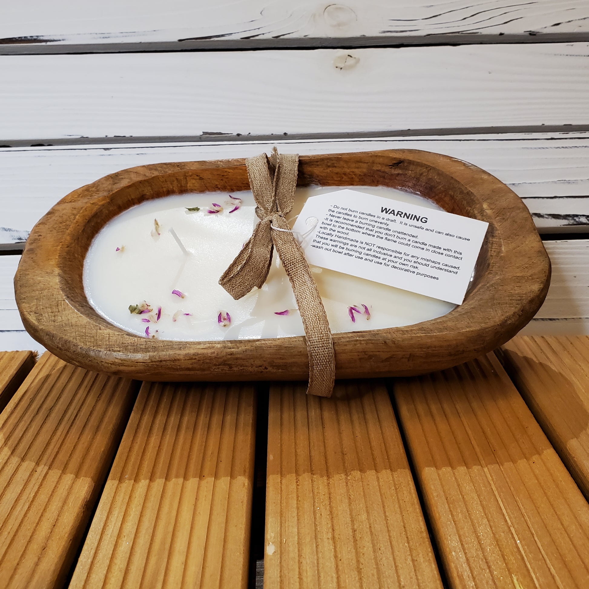 Candle in a wooden dish with a warning label on a wooden surface
