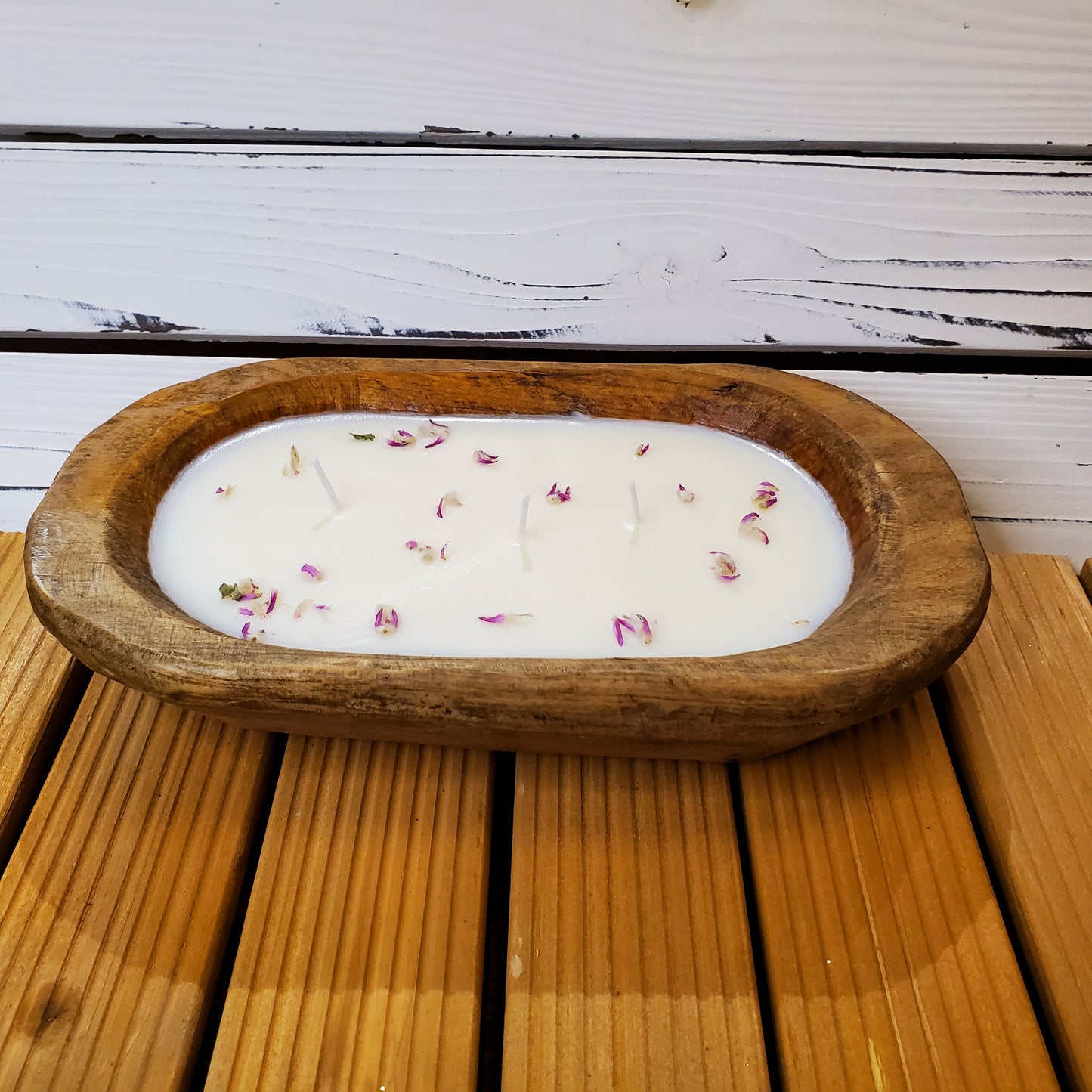 Wooden bowl with a white candle and rose petals on a wooden surface.
