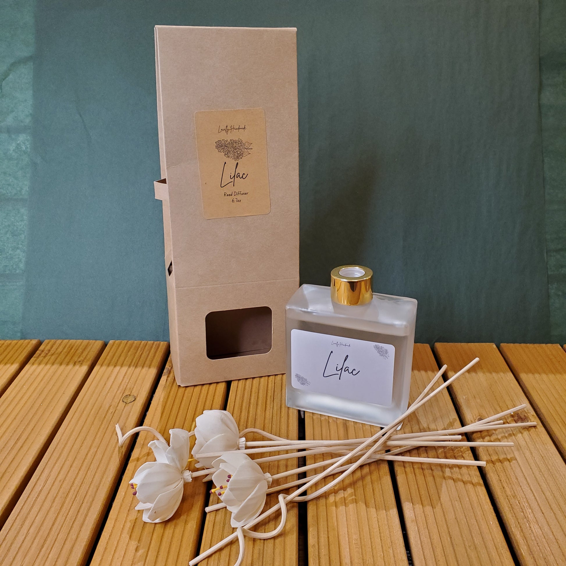 Perfume bottle with gold cap, packaging box, and decorative sticks on a wooden surface.