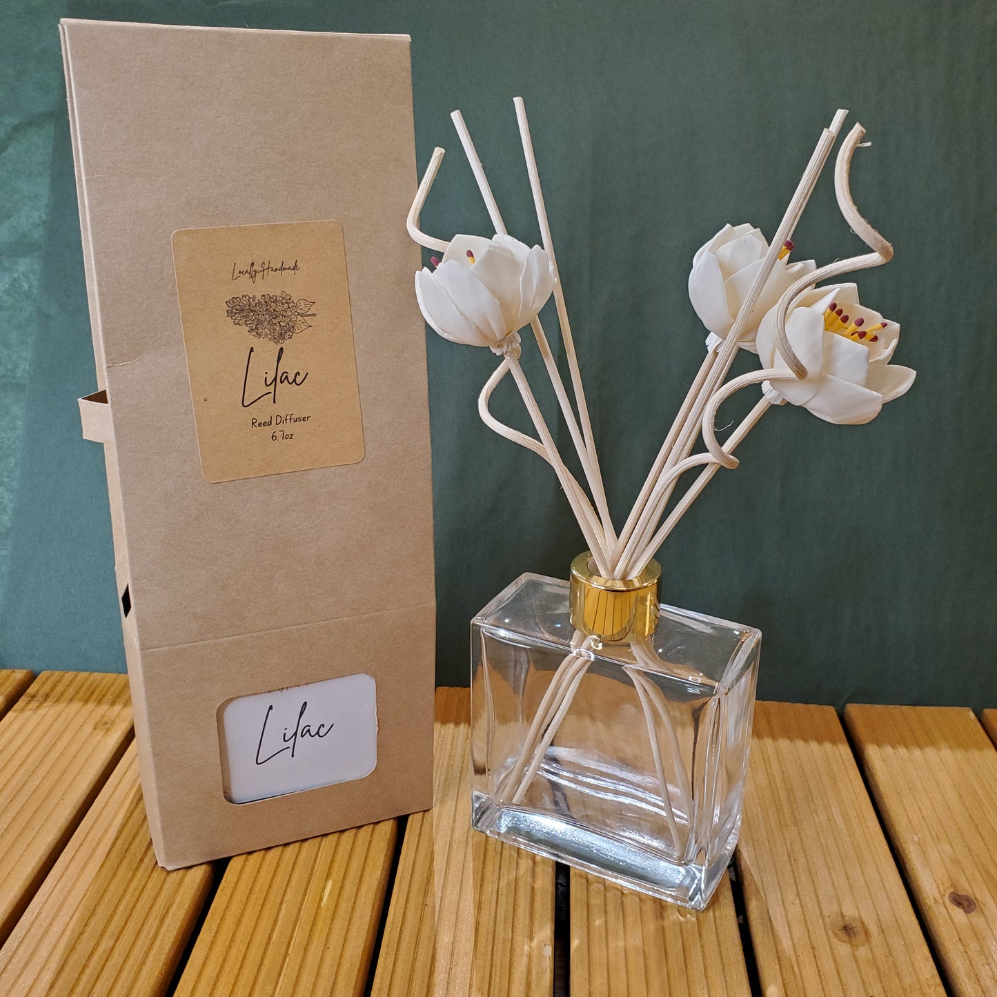 Decorative diffuser with white floral sticks and a clear bottle on a green surface.