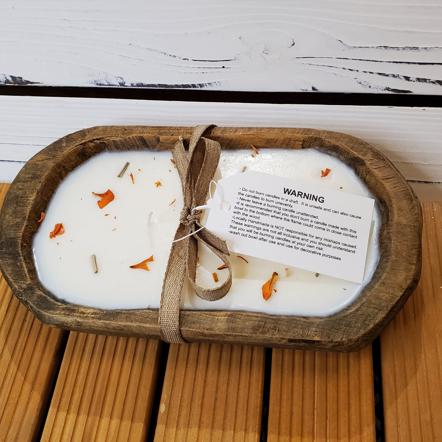 Candle in a wooden dish with a warning label on a wooden surface