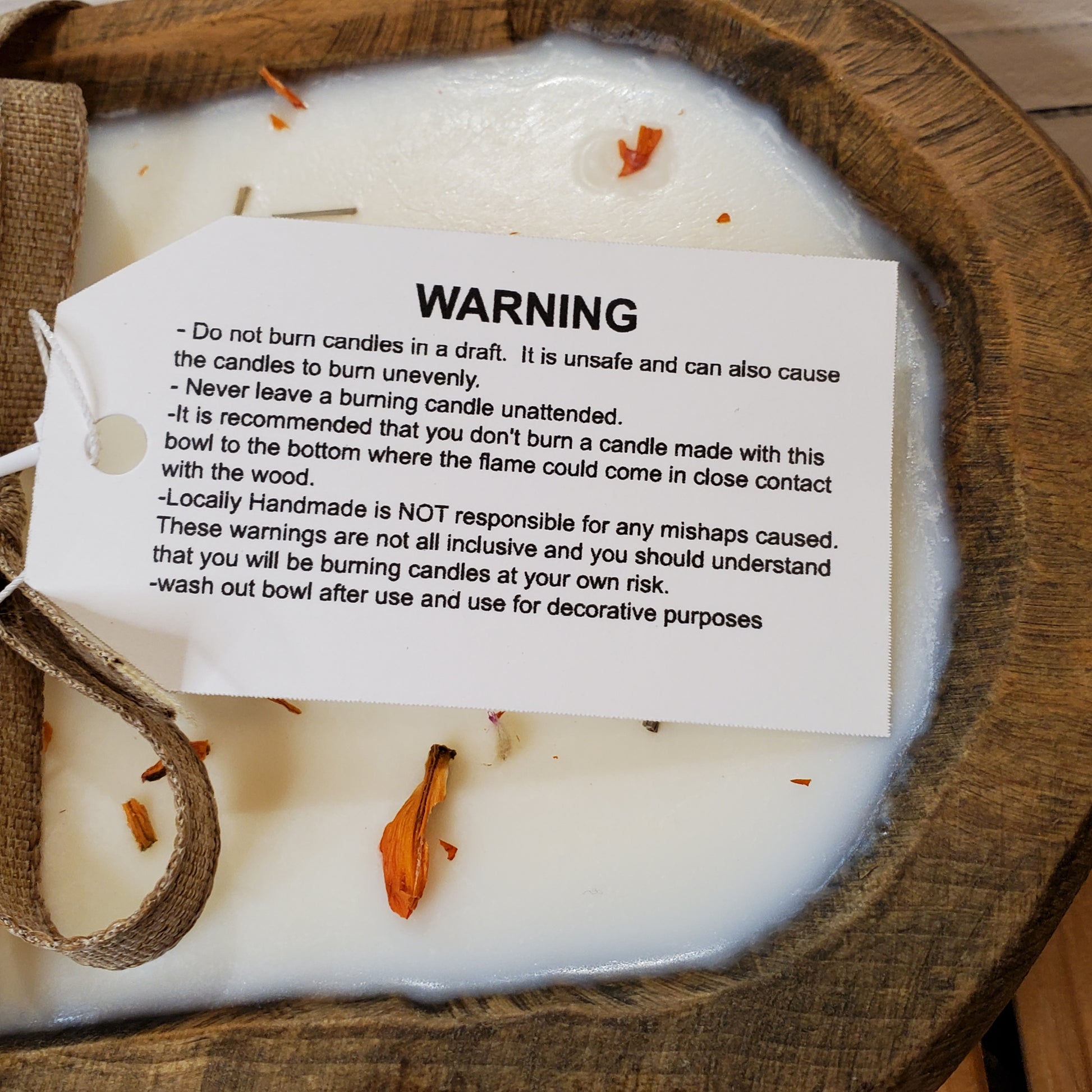 Candle with a warning label on a wooden surface