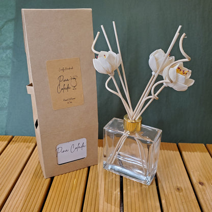 Clear glass diffuser bottle with white floral reeds on a wooden surface