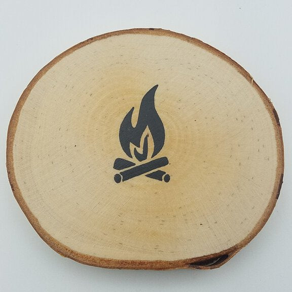 A round coaster made from birch tree wood with a hand-painted campfire design in the center.